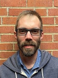 Image of a male standing against a brick wall background. This image would not be accepted for submission.