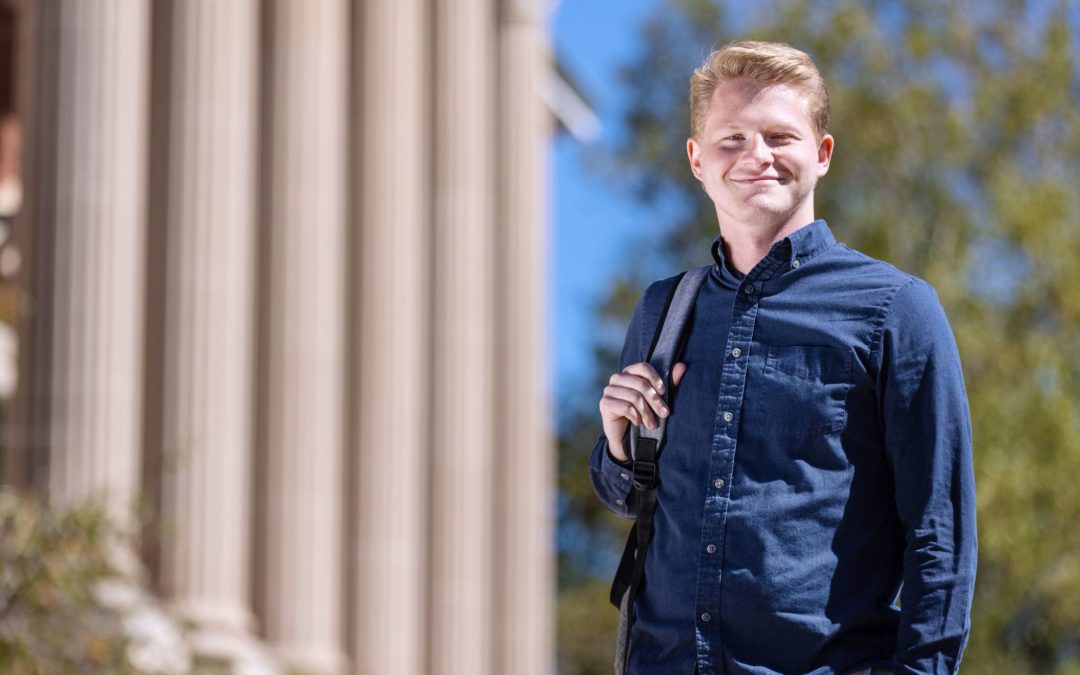 A student with a backpack on one shoulder standing outside