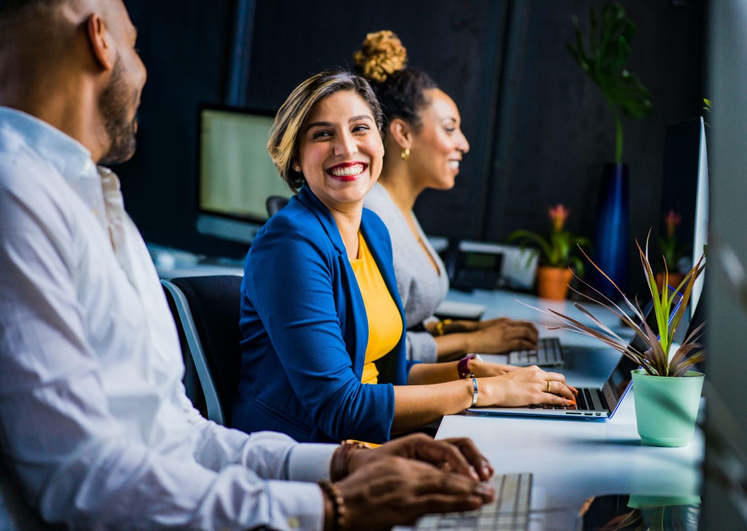 Female business professional working on a laptop laughing with co-workers