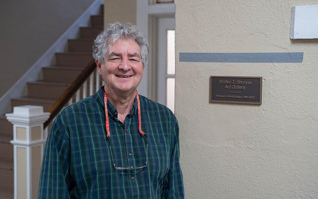 Walter Shroyer beside a plaque that reads "Walter T. Shroyer Art Gallery, Professor of Art & Design, 1991 to 2022".
