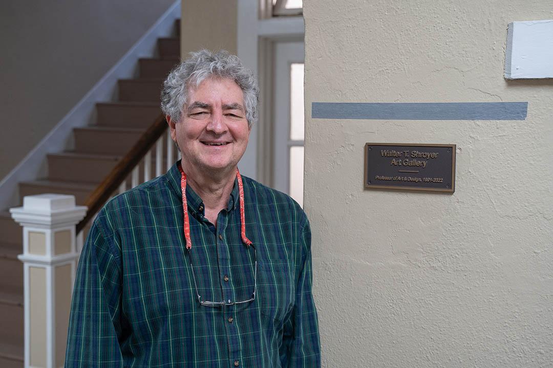 Walter Shroyer beside a plaque that reads "Walter T. Shroyer Art Gallery, Professor of Art & Design, 1991 to 2022".