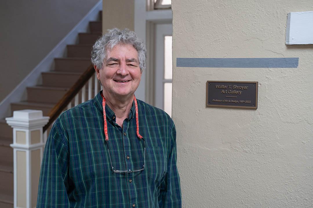 Walter Shroyer beside a plaque that reads "Walter T. Shroyer Art Gallery, Professor of Art & Design, 1991 to 2022".