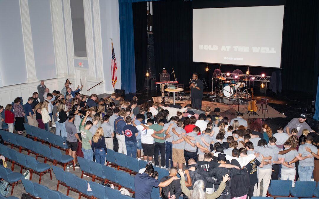 A crowd of people standing in front of the chapel platform, hugging and raising hands.