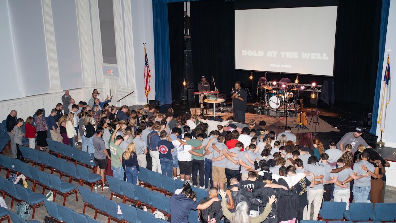 A crowd of people standing in front of the chapel platform, hugging and raising hands.