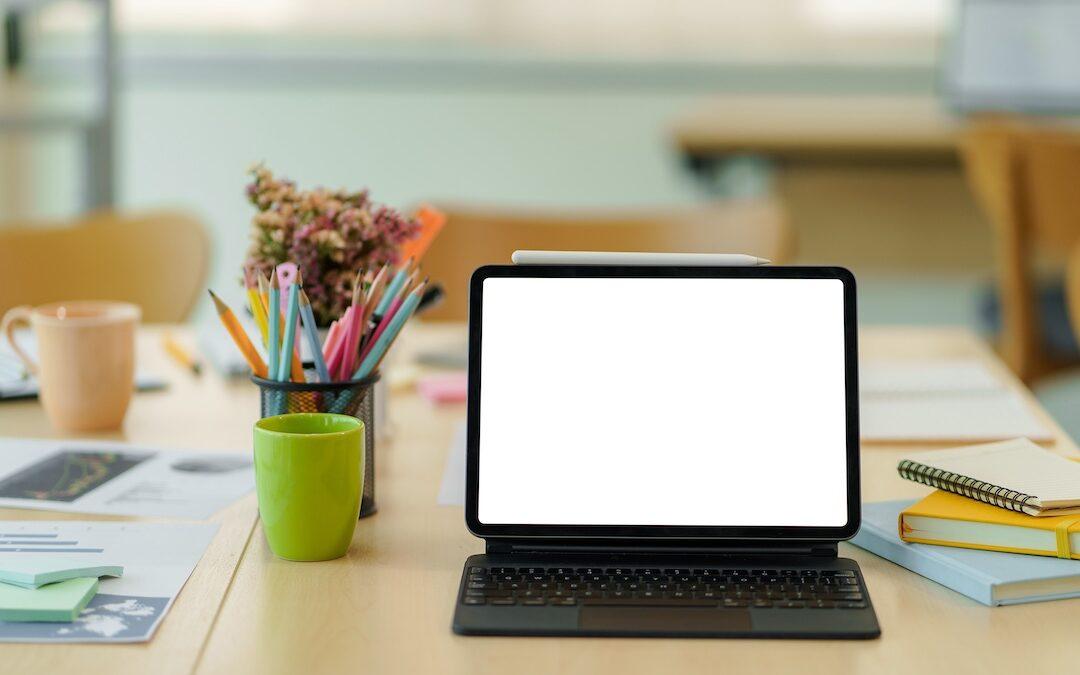 Portable computer with blank screen showing keyboard and stylus pen on wooden table in classroom.