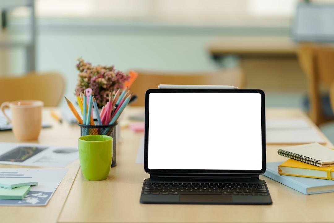 Portable computer with blank screen showing keyboard and stylus pen on wooden table in classroom.