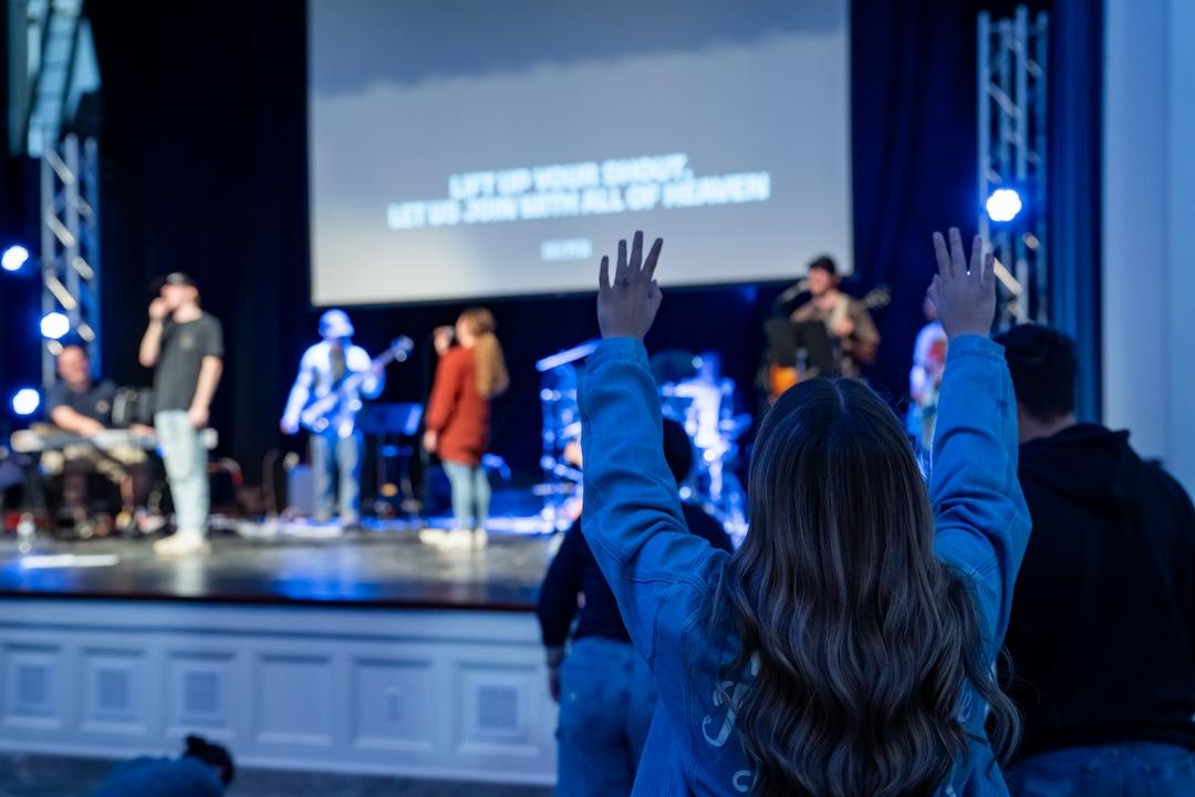 A girl raising her hands while a worship band leads music.