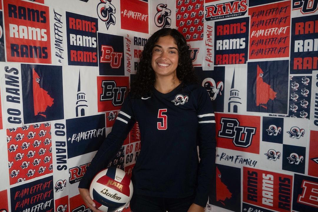 Chesed Russell 2026 A female student holding a volleyball in front of a background of Bluefield University logos.