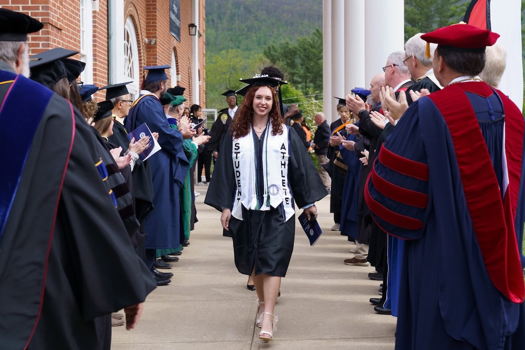 Commencement-2 A female graduate walks through a crowd of faculty